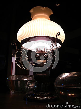 An elegant old-fashioned brass lamp gently shining from the dark corner near my table in the restaurant Stock Photo