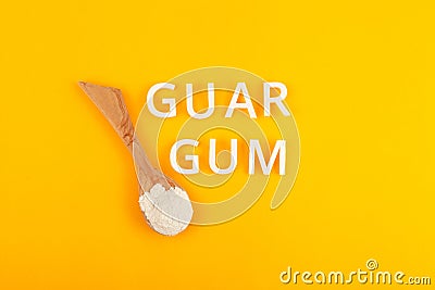Guar gum powder or guaran in wooden spoon on yellow background. Food additive E412. Inscription GUAR GUM. Extract of seed Stock Photo