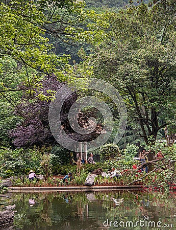 Gardeners and visitors behind pond in Seven Star Park, Guilin, China Editorial Stock Photo