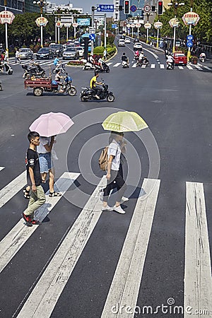 Women with sun umbrellas cross street in downtown Guilin. Editorial Stock Photo