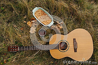 Guitar lying on an autumn green and yellow grass next to a cup of tea and a pie Stock Photo