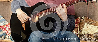 Guitar music lessons at home concept. fingers on a guitar to play arpeggios. Man hands playing black acoustic guitar, wide photo Stock Photo