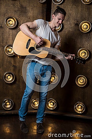 Guitarist, music. A young man plays an acoustic guitar on a background with lights behind him. Vertical frame Stock Photo