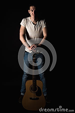 Guitarist, music. A young man stands with an acoustic guitar, on a black isolated background. Vertical frame Stock Photo