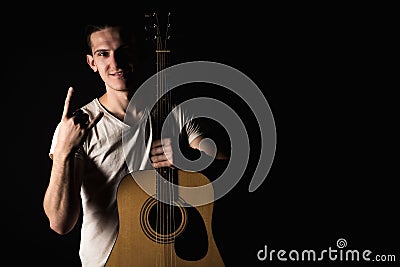 Guitarist, music. A young man stands with an acoustic guitar and shows his fingers, on a black isolated background. Horizontal fra Stock Photo