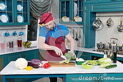 A Guy in apron preparing broccoli. chef cutting broccoli at home kitchen. A man cuts up fresh broccoli on a cutting board. Stock Photo