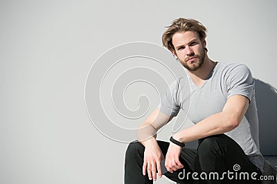 Guy with beard and blond hair in casual tshirt. Macho hold smartphone on sunny outdoor. Bearded man with mobile phone on grey wall Stock Photo