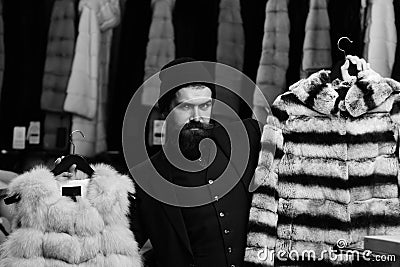 Guy with beard chooses furry coats. Elegance and glamour concept. Man with serious face Stock Photo