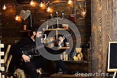 Guy in cozy warm atmosphere play relaxing soul music. Man bearded musician enjoy evening with bass guitar, wooden Stock Photo