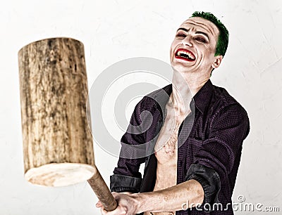 Guy with crazy joker face, green hair and idiotic smile. carnaval costume. holding hammer for cricket Stock Photo