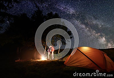 Guy and girl kissing by the fire under bright starry sky which is visible milky way near tent in woods Stock Photo