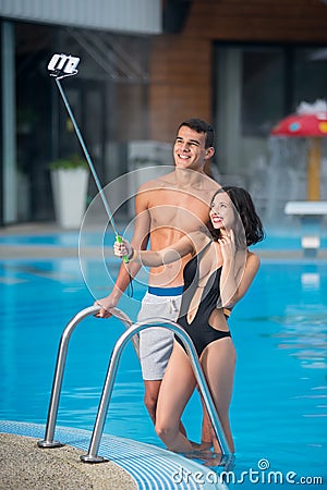 Guy and girl posing against the swimming pool with perfect aqua water and taking selfie photo with monopod on the resort Stock Photo