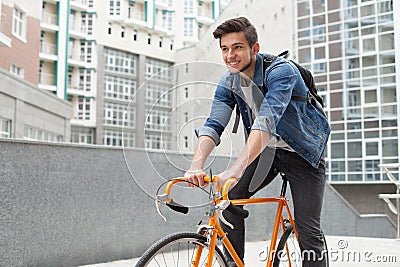 The guy goes to town on a bicycle in blue jeans jacket . young man an orange fix bike Stock Photo