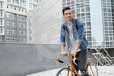 The guy goes to town on a bicycle in blue jeans jacket . young man an orange fix bike Stock Photo