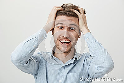 Guy is going crazy. Weird funny attractive male in casual blue shirt holding hands on hair and smiling with strange Stock Photo