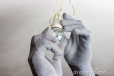 A guy in gray gloves is spinning a light bulb. Replacing the light bulb. Stock Photo