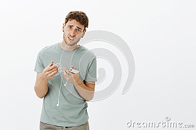 Guy hate when earphone wire knotting. Portrait of fed up displeased handsome man with fair hair, holding earbuds and Stock Photo