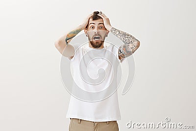 Guy heard horrible news, being very shocked. Portrait of nervous stunned emotive bearded man in white t-shirt, holding Stock Photo
