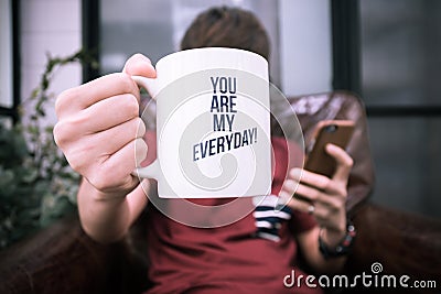 A guy hold coffee cup with word you are my everyday and playing smartphone Stock Photo