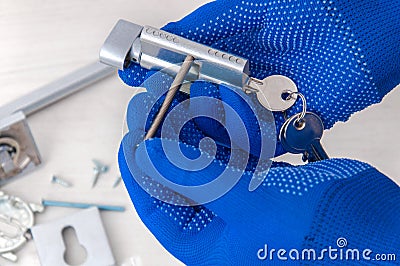 The guy holds in his hands in blue gloves the core of the lock and door keys on a light background. Stock Photo