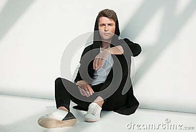 Guy with the hoodie is sitting against the white wall. Stock Photo