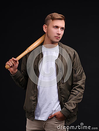 A guy in a jacket, stands and holds a bat on his shoulder. On a black background. Stock Photo