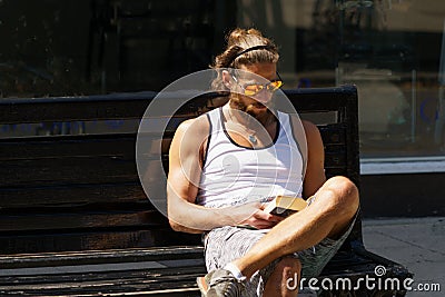 Guy Reading a Book While Relaxing on a Bench. Editorial Stock Photo