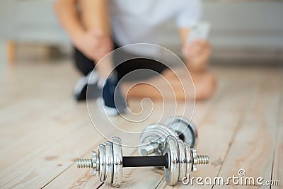 Guy in sportswear and sneakers, sits on floor and types at smartphone in interior with dumbbells Stock Photo