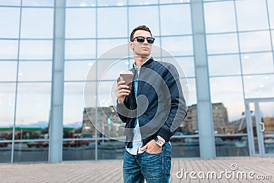 The guy in stylish sunglasses, a man walks around the city and drinking coffee from a paper Cup, a handsome guy walks around and r Stock Photo