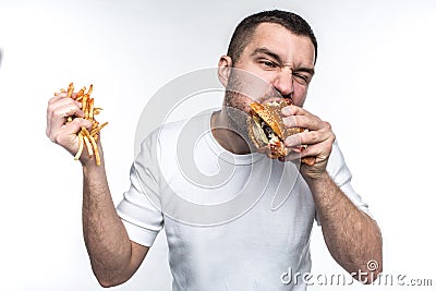 This guy is very delight of junk food. He is biting a big piece of burger and holding a full hand of french fries Stock Photo