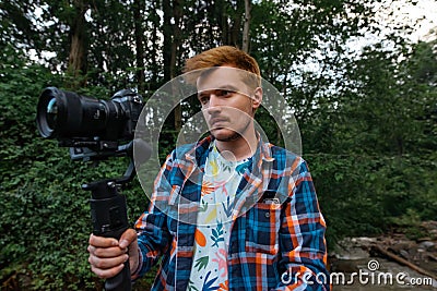 Guy a video maker with a camera on a stabilizer in his hands stands in the Greek forest and shoots video content for a travel blog Stock Photo