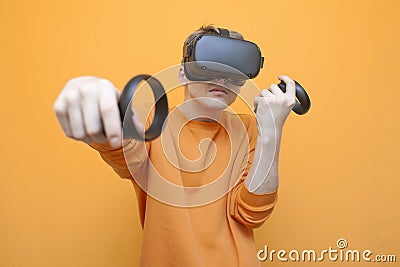 Guy in VR glasses on an orange background, a gamer holds joysticks and plays a virtual shooter Stock Photo