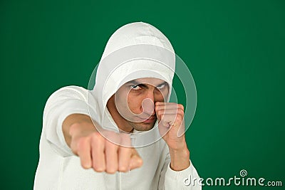 a guy in a white hoodie on a green chromakey background hits the camera with his fist a stern angry look defense attack Stock Photo