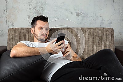 The guy in the white shirt is lying on the couch and sitting in the phone. The concept of laziness, apathy Stock Photo