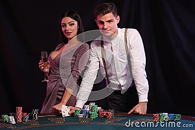 Guy in white shirt is playing poker at casino, at table with stacks of chips on it. He celebrating win with sexy female Stock Photo