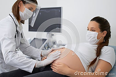 Gynecologist in mask doing palpation of pregnant woman Stock Photo