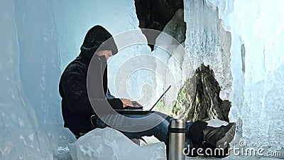 Hacker hacks the server. Man to program on laptop in ice cave. Around the mysterious ice grotto. Man hides himself in a Stock Photo