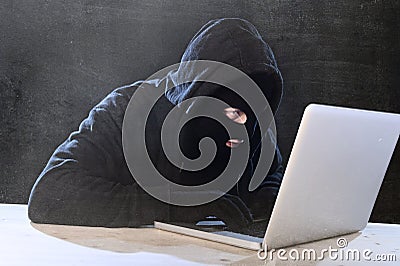 Hacker man in black hood and mask with computer laptop hacking system in digital intruder cyber crime concept Stock Photo