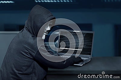 Hacker man wearing mask using laptop to upload computer virus Editorial Stock Photo