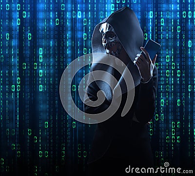 a hacker in a scary mask and hood stands against the background of a digital binary code Stock Photo