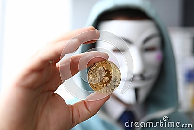 Hacker wear anonymus mask hold bitcoin in hand Editorial Stock Photo