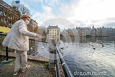 The Hague, The Netherlands - November 10, 2020: Cityscape of The Hague. Happy elderly senior retired woman feeds birds. She wears Editorial Stock Photo