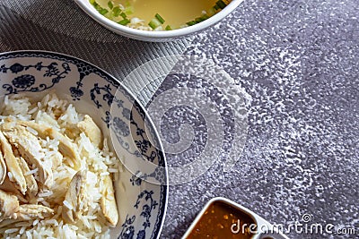 Hainanese chicken rice served in a Chinese style dish with soy sauce and broth on a gray table Stock Photo
