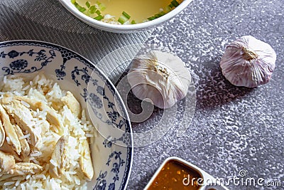 Hainanese chicken rice served in a Chinese style dish with soy sauce and broth on a gray table Stock Photo