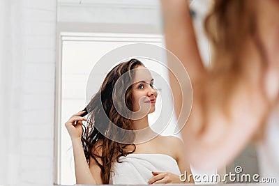 Hair and body care. Woman touching wet hair and smiling while looking in the mirror. Portrait of girl in bathroom applying condit Stock Photo