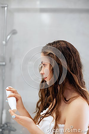 Hair and body care. Woman touching wet hair and smiling while looking in the mirror. Portrait of girl in bathroom applying condit Stock Photo