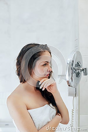 Hair and body care. Woman touching wet hair and smiling while looking in the mirror. Portrait of girl in bathroom applying condit Stock Photo