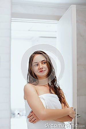 Hair and body care. Woman touching wet hair and smiling while looking in the mirror. Portrait of girl in bathroom applying condit Stock Photo