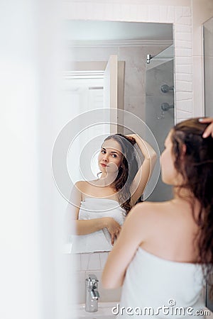 Hair and body care. Woman touching wet hair and smiling while looking in the mirror. Portrait of girl in bathroom applying condit Stock Photo