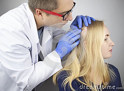 A doctor trichologist conducts a study of the hair of a blonde. Alopecia treatment. Hair loss, alopecia, itching, burning in the Stock Photo